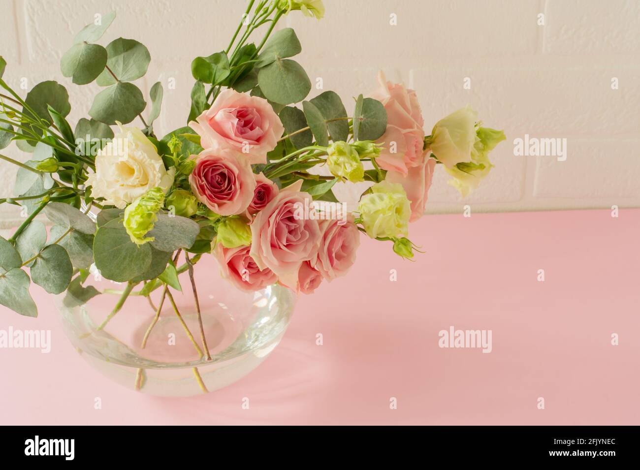 Vase mit schönen Rosen, Eustoma und Eukalyptusblumen auf dem Tisch. Zarte Grußkarte für den Urlaub. Stockfoto