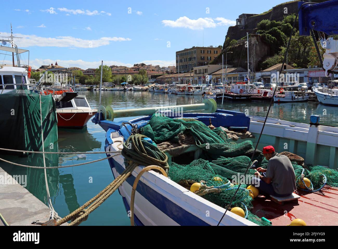 Ein Fischer flicken Netze auf seinem Boot im alten Hafen von Korfu, unter einer Mauer der Neuen Festung, rechts vom Rahmen. Blick in Richtung Altstadt von Korfu Stockfoto