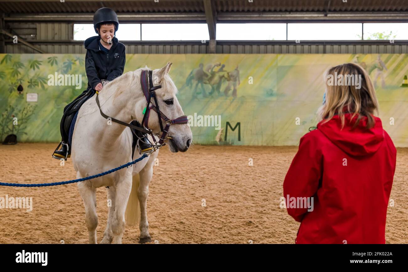 East Lothian, Schottland, Großbritannien, 27. April 2021. Muirfield Riding Therapy wird wieder eröffnet: Die Wohltätigkeitsorganisation begrüßt ihre ersten Jugendlichen zu ihrer Therapiestunde mit Lockdown-Einschränkungen. Aufgrund der anhaltenden Einschränkungen können derzeit nur die mobilen Clients bedient werden, die immer mehr Kunden betreuen. Im Bild: Nathan, 10 Jahre alt, Schüler der Yester Primary School auf seinem Therapiepferd Johnny, der von Trainer Shirley Duff unterrichtet wurde Stockfoto