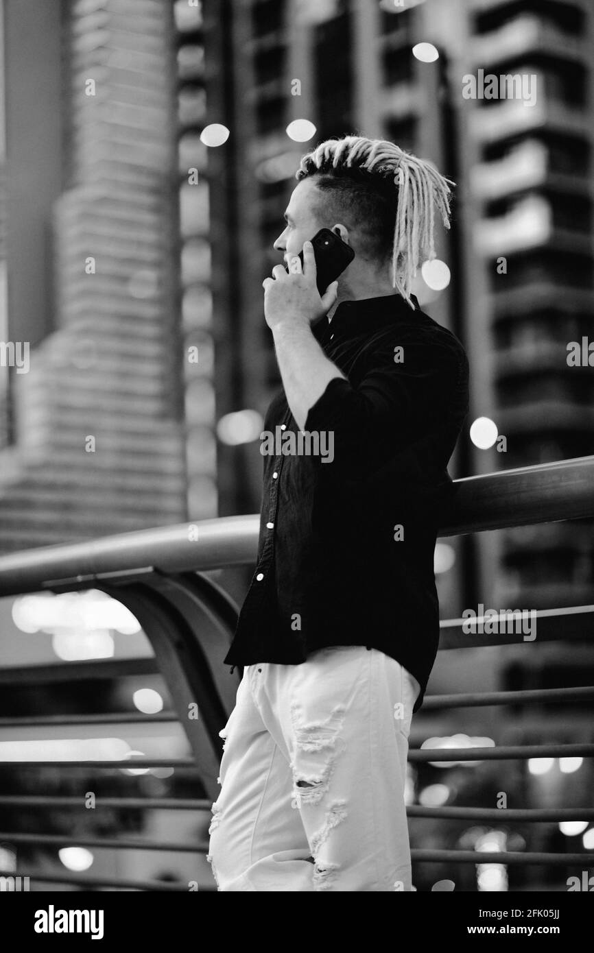 Schwarz-Weiß-Porträt des modernen Geschäftsmannes mit moderner Frisur Spricht per Smartphone vor dem Hintergrund der Megapolis Stockfoto