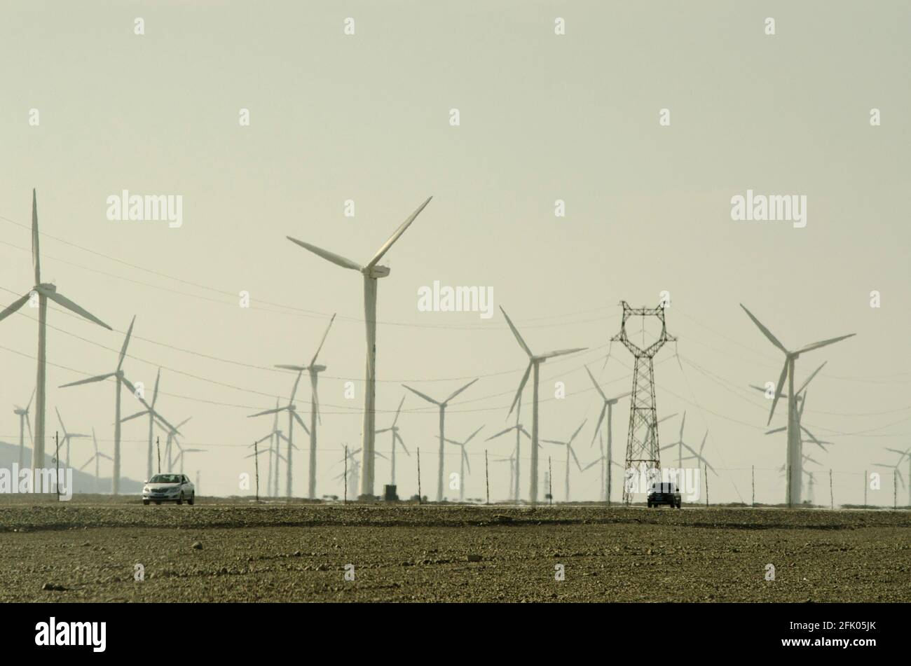 Autos fahren im schimmernden Dunst entlang des G312 Highway, vorbei an Windkraftanlagen und Stromleitungen, die die Wüste am westlichen Stadtrand von Turpan durchqueren, an einem der heißesten Orte der Welt. Erneuerbare Energie aus Wind wird von den Chinesen zunehmend zum Ausbau ihrer stromhungrigen Industrien genutzt, wie hier in OstXinjiang, China, VR China, zu sehen ist. © Time-Snaps Stockfoto