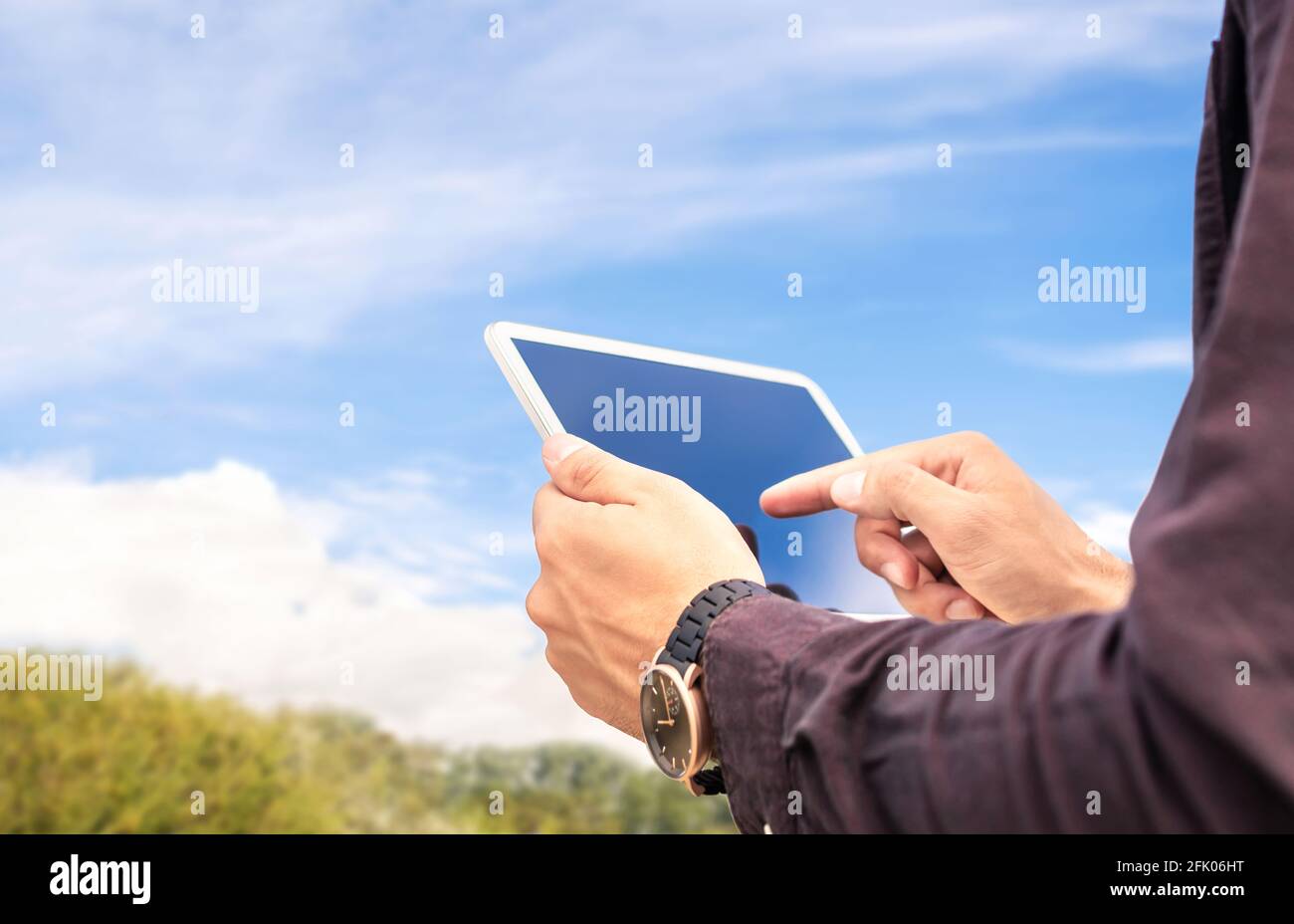Tablet in der Natur im Freien. Bauernhof oder Garten mit blauem Himmel und Wolken. Mann, der ein Smart-Gerät im Freien verwendet. Grünes Grasfeld oder Park im Hintergrund. Stockfoto
