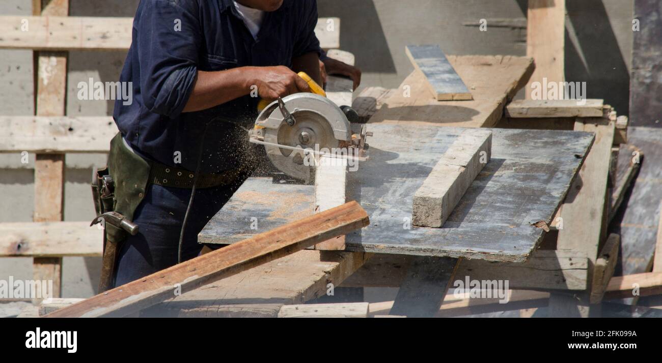 Bauarbeiter schneiden mit Kreissäge mit Arbeitskleidung und Werkzeugen. Blaue Overalls, gelber Helm, Schutzbrille, um Werkzeuge sicher verwenden zu können Stockfoto