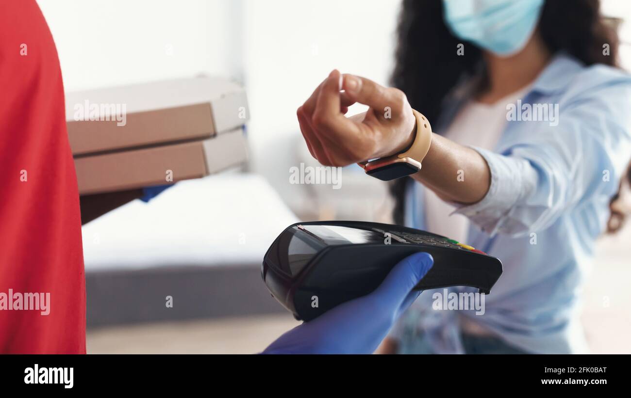 Einfaches Kontaktloses Pay-Konzept. Nahaufnahme des Lieferers in Schutzhandschuhen mit Zahlungsterminal und Pizzakartons, Frau in medizinischer Chirurgie Stockfoto