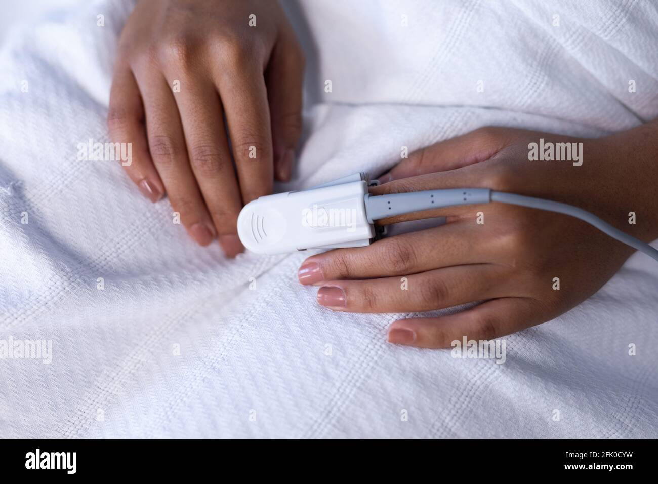 Mittelteil einer weiblichen Patientin mit gemischter Rasse im Krankenhausbett Pulsoximeter mit Fingerspitze Stockfoto