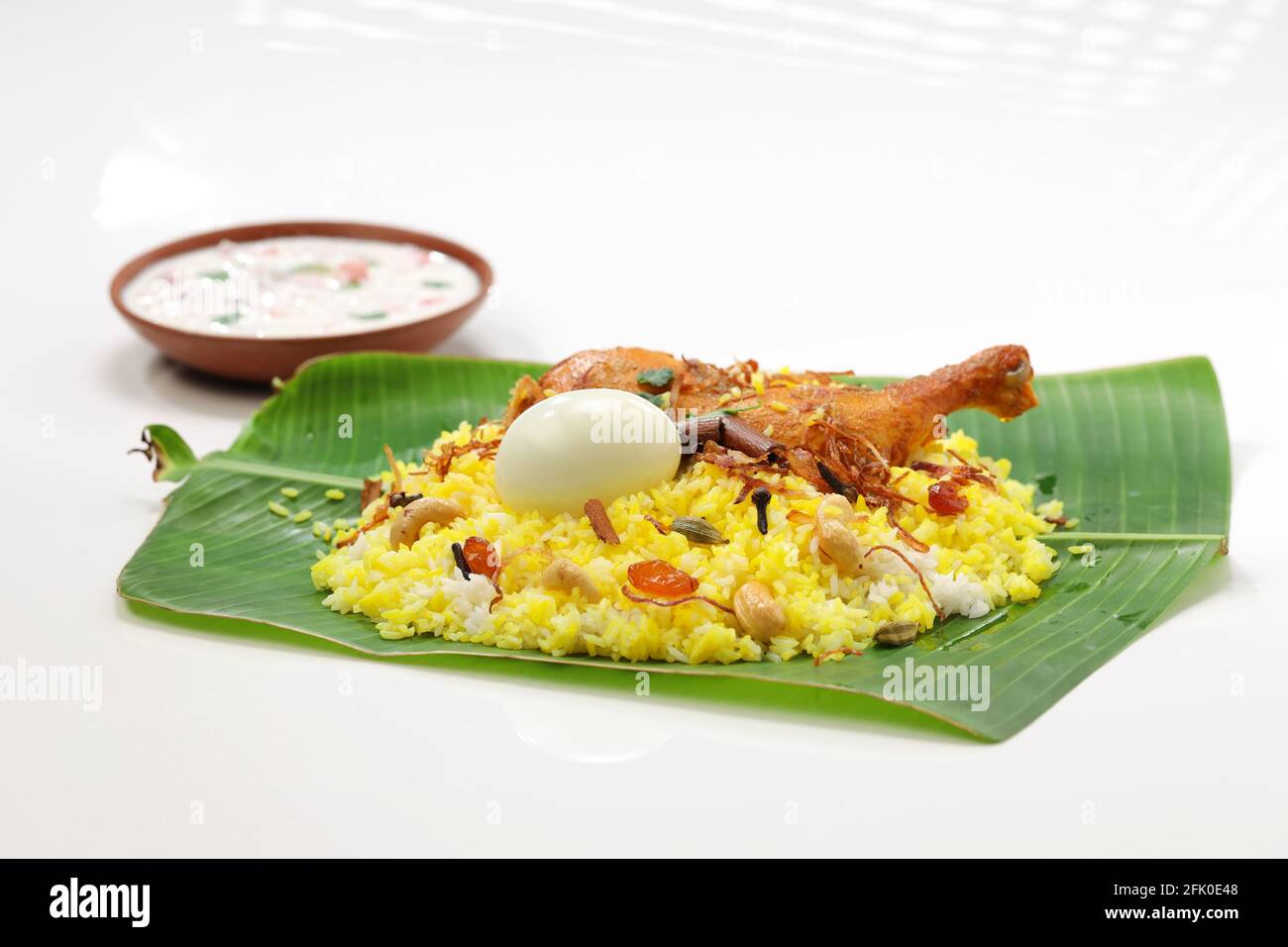 Kerala Chicken dum biryani, traditionell in einem Bananenblatt angeordnet Und Raita als Beilage mit weißem Hintergrund oder Textur, selektiv Fokus Stockfoto