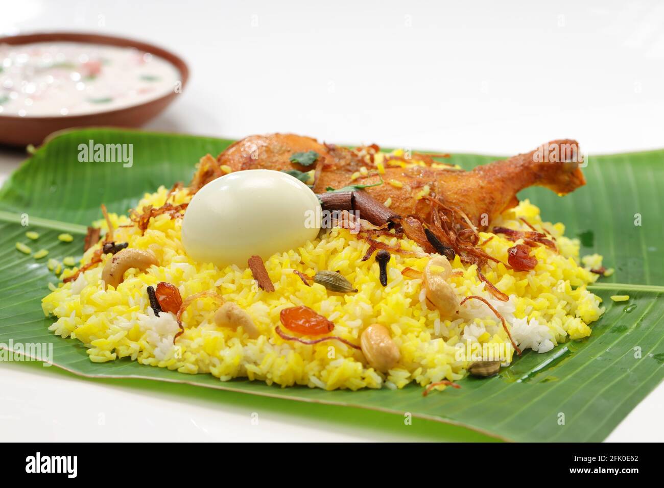 Kerala Chicken dum biryani, traditionell in einem Bananenblatt angeordnet Und Raita als Beilage mit weißem Hintergrund oder Textur, selektiv Fokus Stockfoto