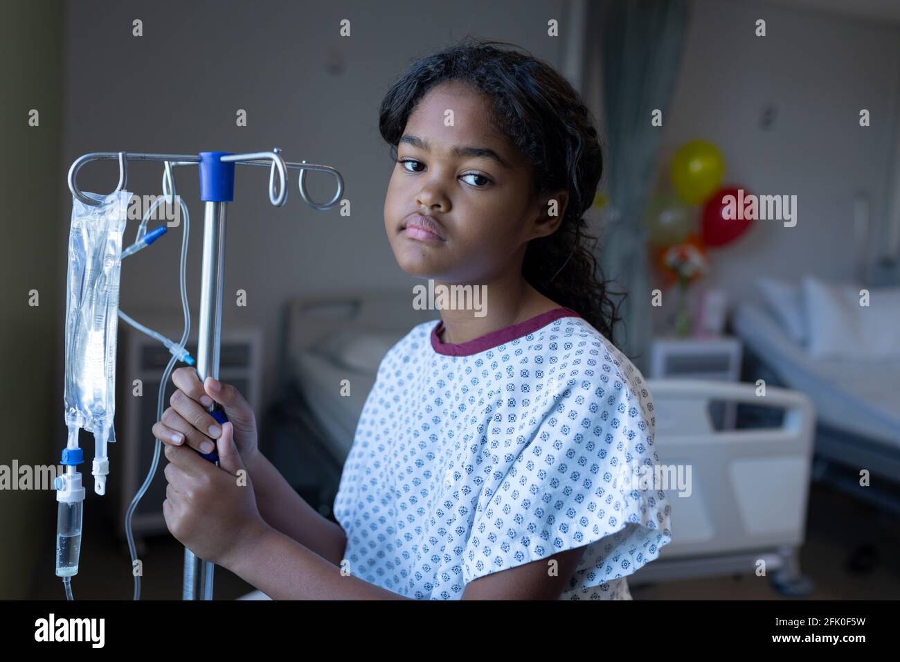 Porträt eines gelangweilten kranken Mädchens mit gemischter Rasse, das im Krankenhaus steht Station mit infusionsbeutel auf Stativ Stockfoto