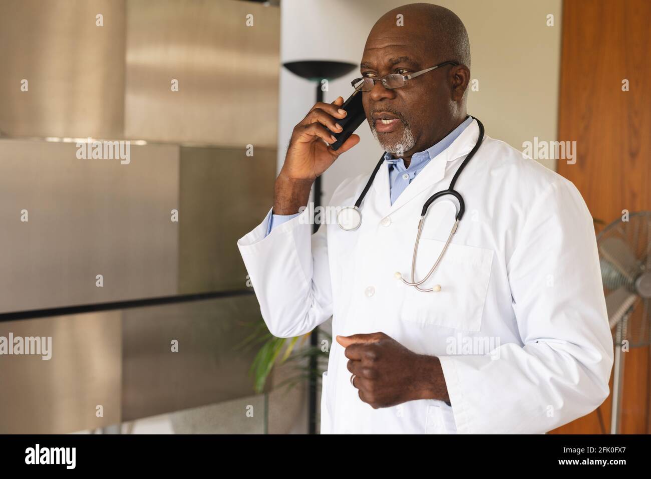 afroamerikanischer leitender männlicher Arzt, der zu Hause auf dem Smartphone spricht Stockfoto