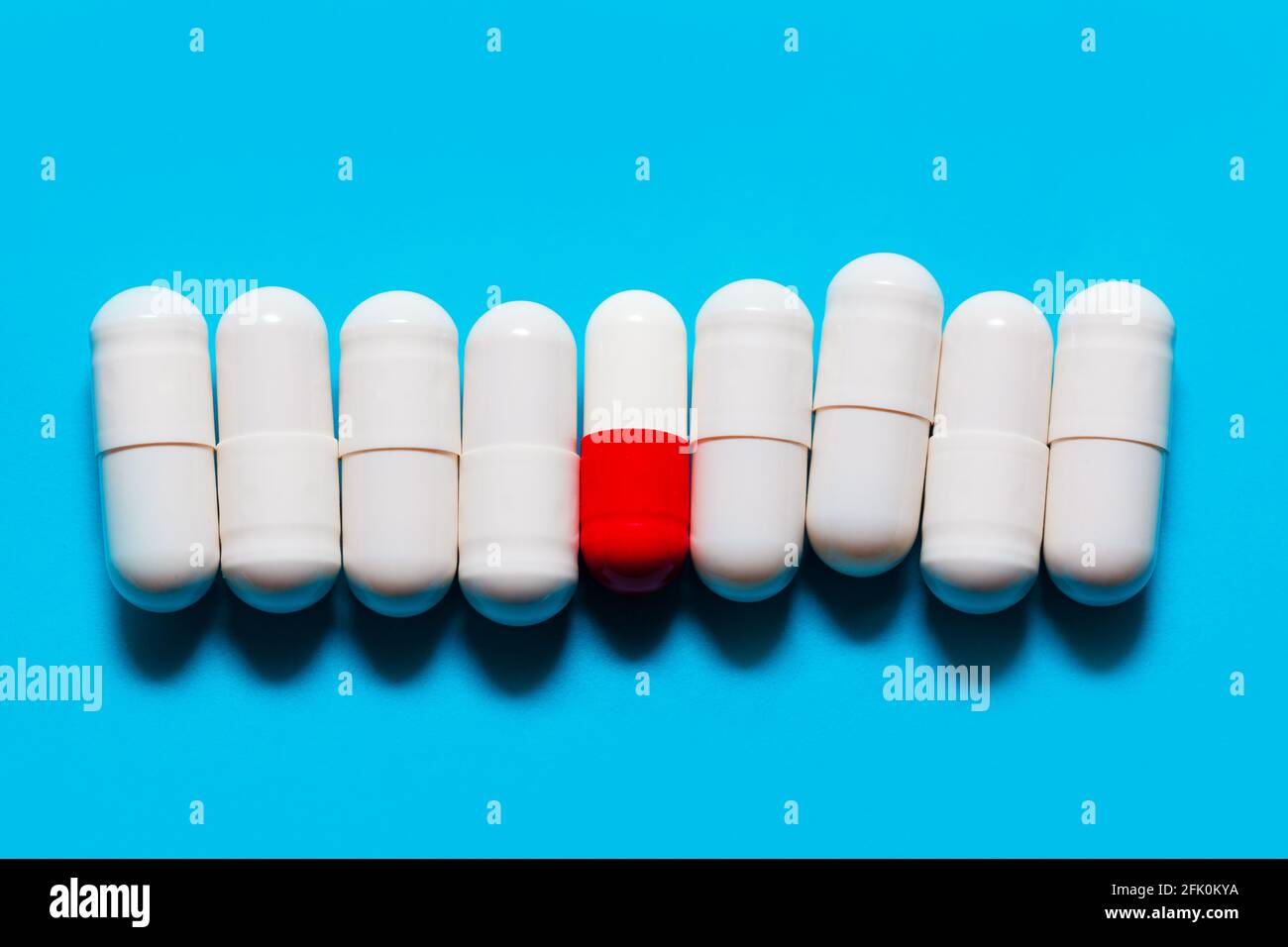 Weiße Probiotische Kapseln . Eine rote und weiße Kapsel zwischen weißen Kapseln . Drogen auf blauem Hintergrund . Pillen in einer Reihe Stockfoto