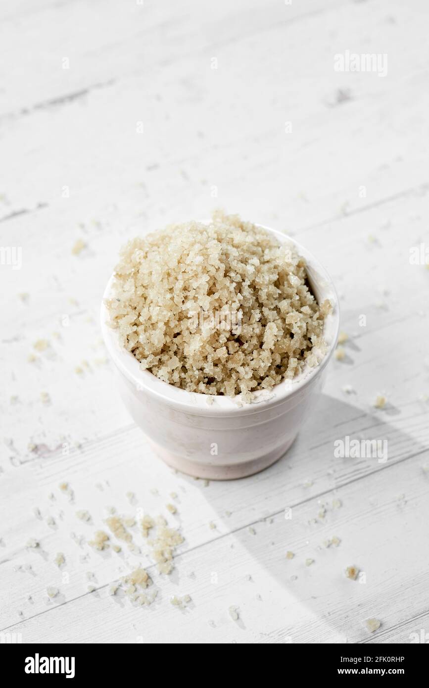 Nahaufnahme eines grauen keltischen Meersalzes in einer weißen Keramikschale auf einem weißen Holztisch Stockfoto