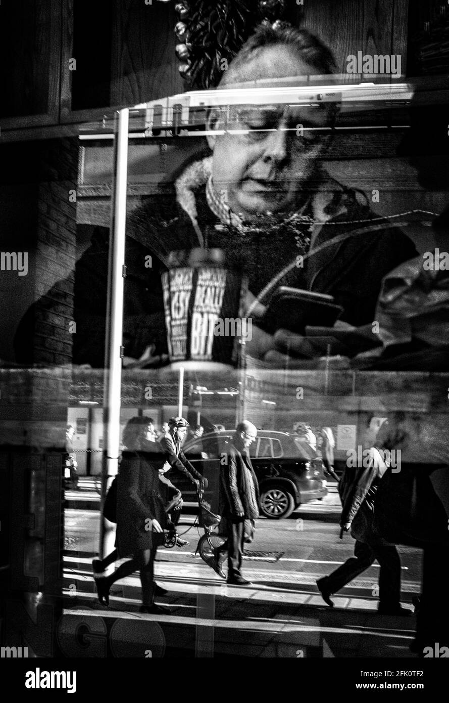 Ein Mann mittleren Alters sitzt im Fenster eines Cafés, während Pendler an den Fenstern der London Bridge vorbeilaufen. Stockfoto