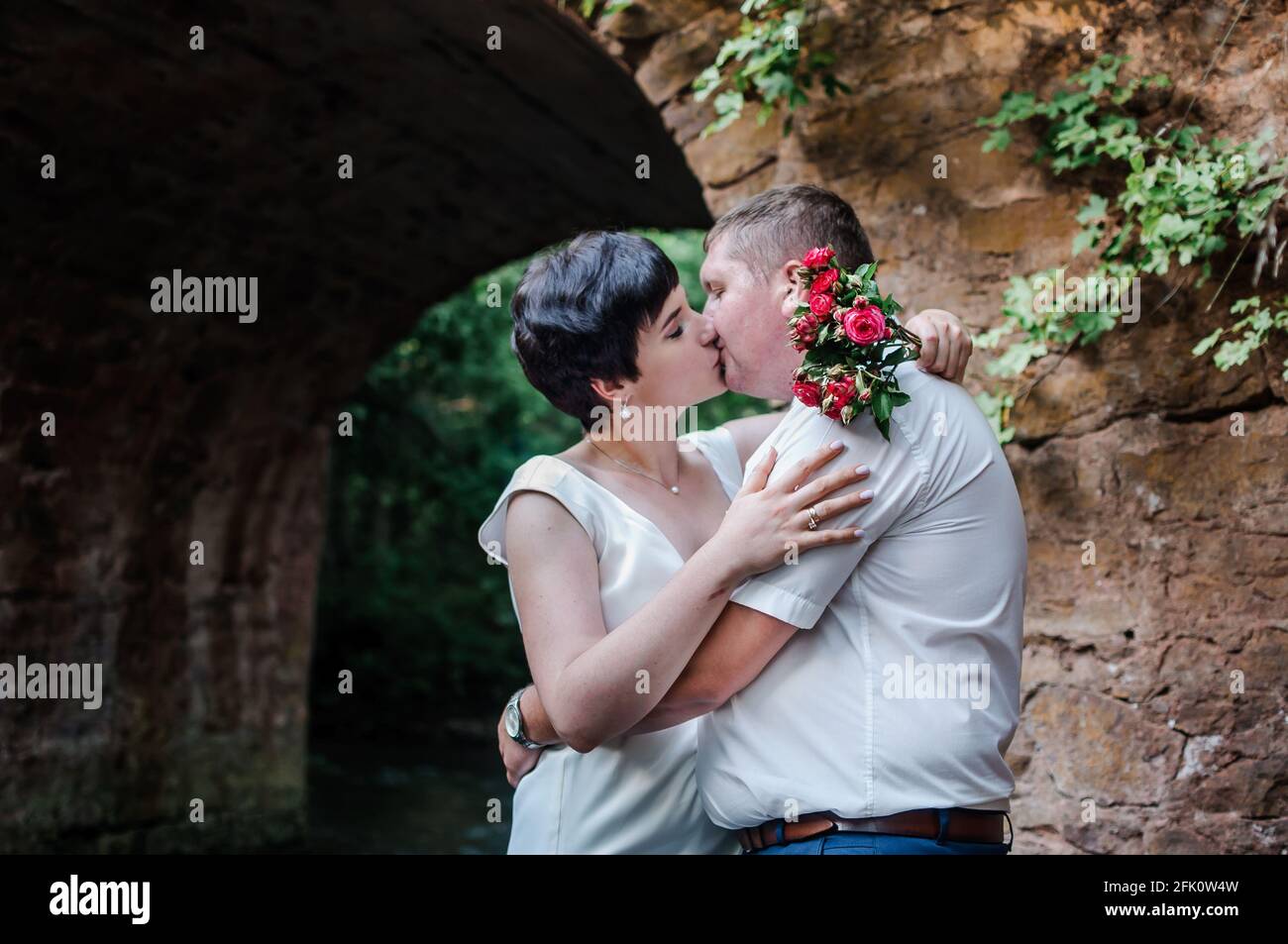 Brautpaar umarmen und küssen vor dem Hintergrund von Wasser und Ein Steinbogen Stockfoto