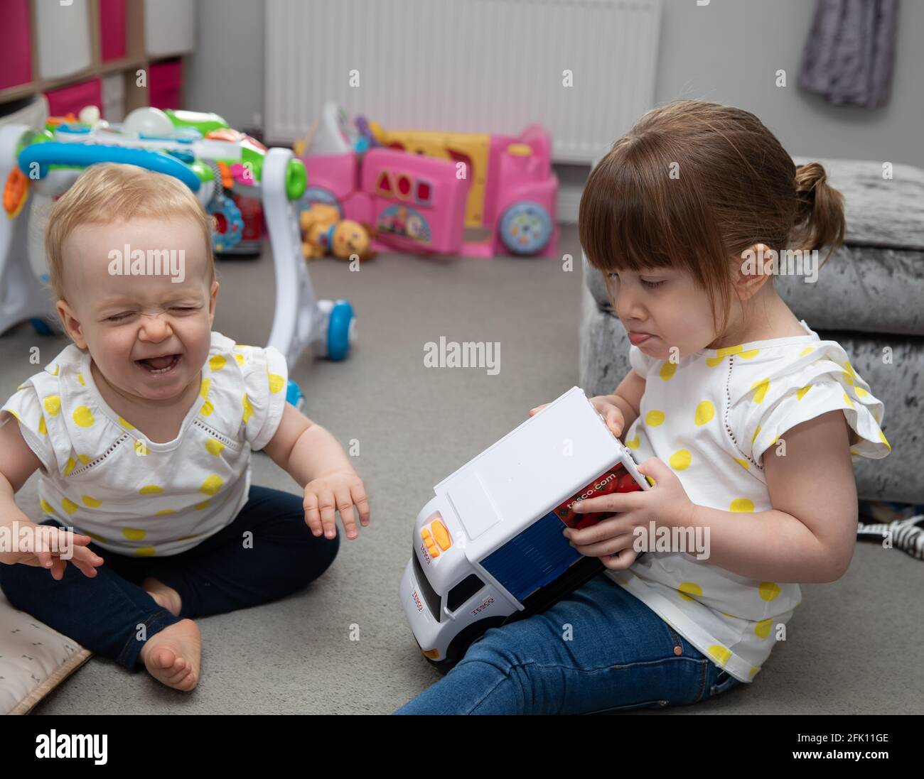 Ein kleines Kind weint, wie ein älteres Kind einen nimmt Spielzeug weg von ihr Stockfoto