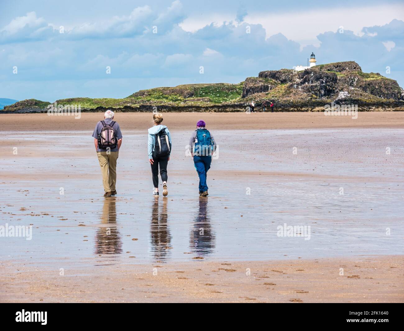 Drei Personen, die im Sommer bei Sonnenschein am Sandstrand von Yellowcraig mit Blick auf Fidra Island und den Leuchtturm, East Lothian, Schottland, Großbritannien, spazieren gehen Stockfoto