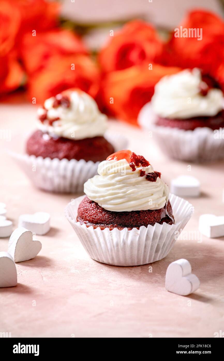 Hausgemachte rote Samt-Cupcakes mit Schlagsahne, weiße Serviette mit Band, Rosenblumen, Holzherzen auf rosa Textur Hintergrund. Valentinstag d Stockfoto