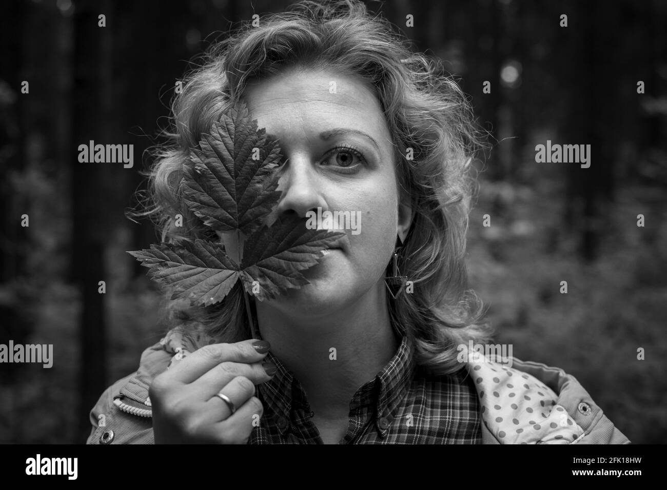 Die blonde Frau bedeckt ihre Augen mit grünen Blättern. Schwarz und Whait Foto. Stockfoto