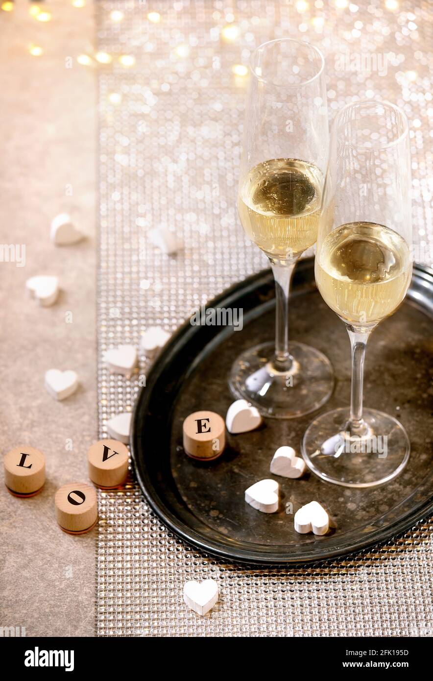 St. Valentine oder Hochzeit Grußkarte mit zwei Champagner Gläser auf Tablett stehen auf silbernen funkelnden Tisch, weiße Herzen, Bokeh Lichter. Liebe Schreibschrift Stockfoto