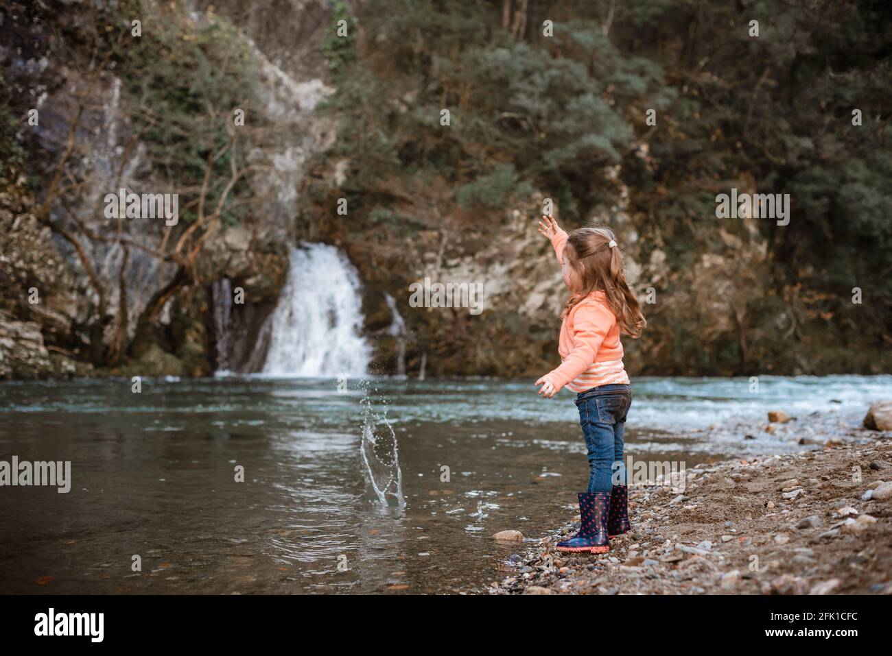 Mädchen wirft Stein in den Fluss vor dem Wasserfall Stockfoto