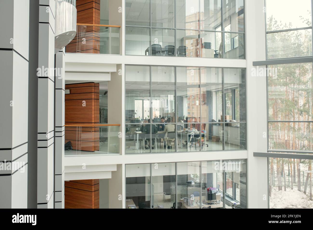 Mehrere Stockwerke mit gläsernen Büroräumen und Holzwänden in den Fluren des modernen Business-Centers, Personen, die im Büro arbeiten Stockfoto