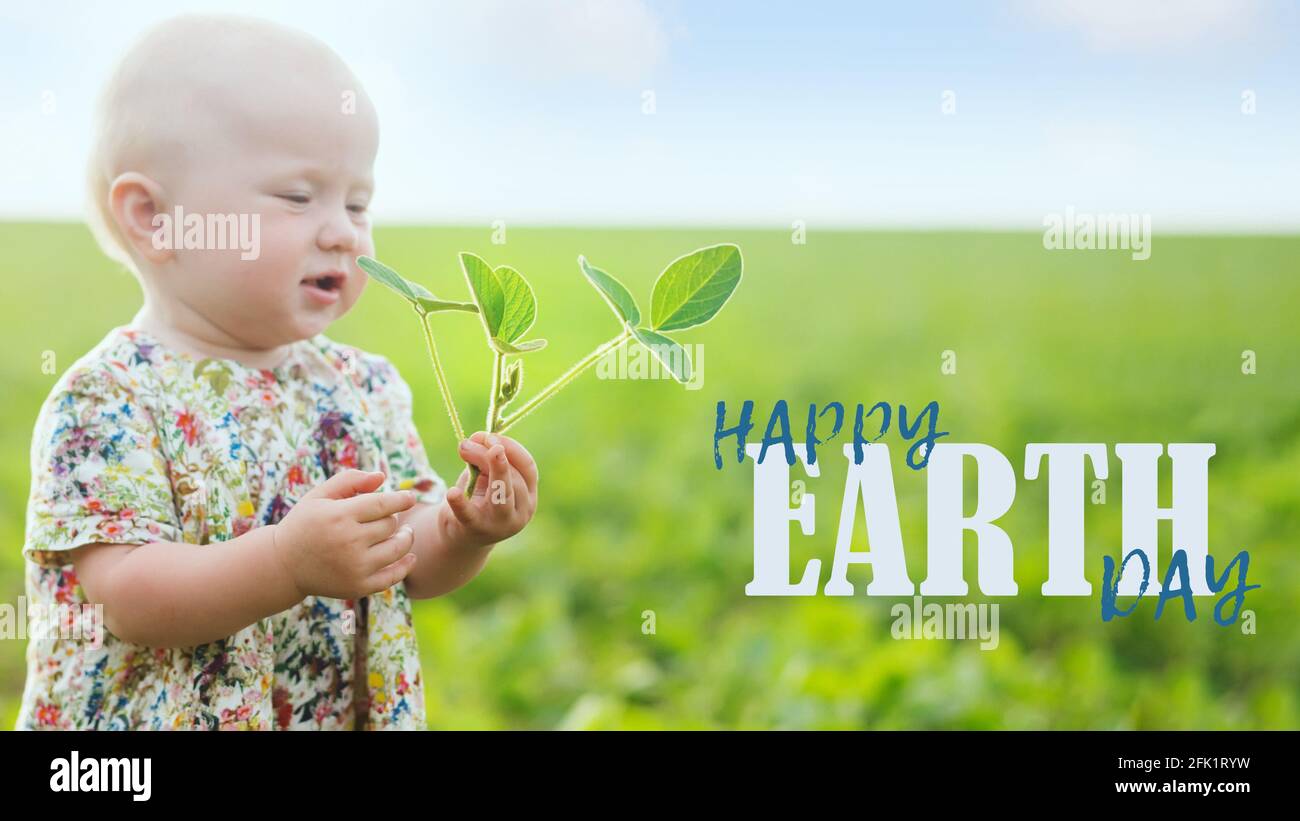 Kleines Mädchen hält jungen Sojabohnensprossen. Text HAPPY Earth Day. Nachhaltige Umwelt, Pflanze Glycine max, Sojabohnen, Sojabohnen Sprossen wachsen Sojabohnen o Stockfoto