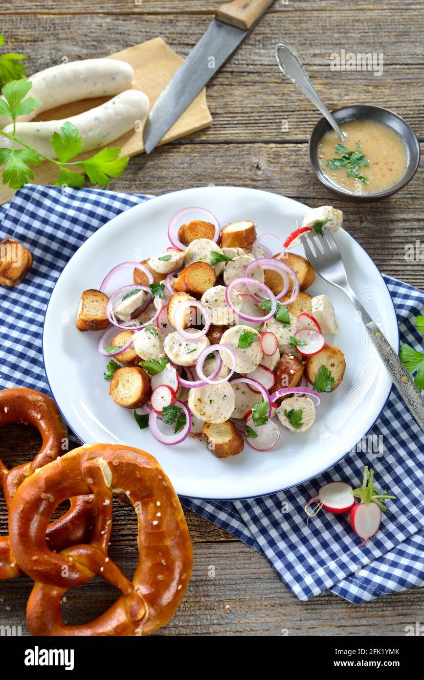 Herzhafter bayerischer Salat mit geschnittenen Kalbswürsten, gebratenen Brezelscheiben und einem Senfdressing auf einem rustikalen Holztisch Stockfoto