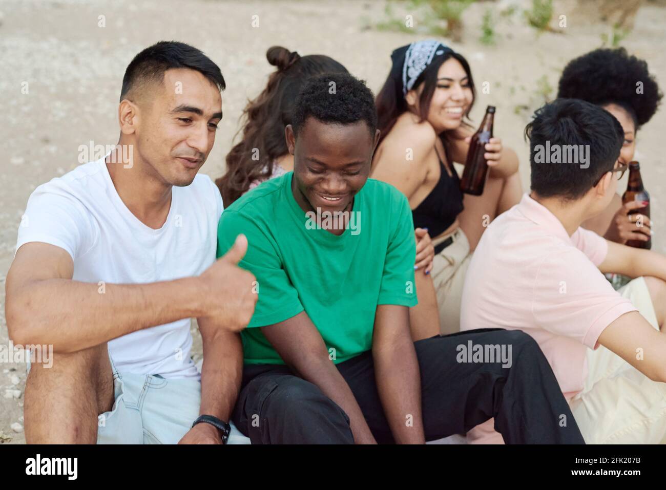 Eine Gruppe von fröhlichen Freunden, die in Sommerkleidung gekleidet sind und am Strand mit Bierflaschen rösten. Stockfoto