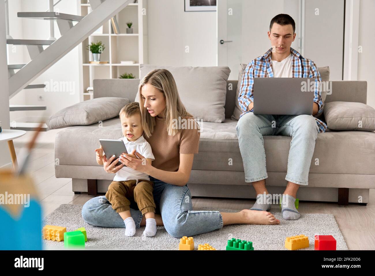 Junge Familie zu Hause, Mama und Kind schauen sich Filme auf dem Tablet an, Papa arbeitet am pc. Stockfoto