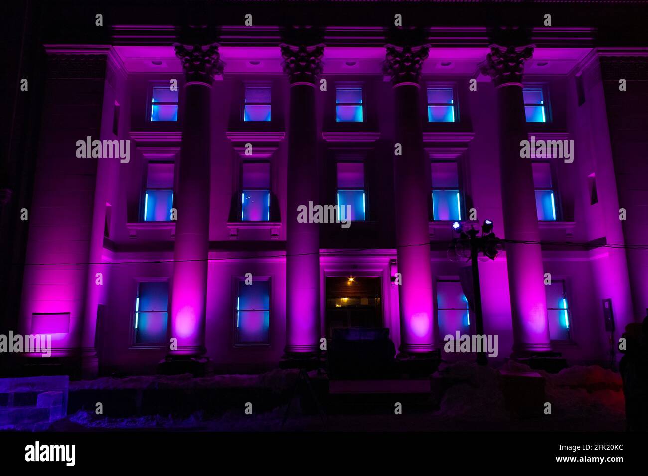 Vierstöckiges Gebäude mit römischen Säulen, die nachts beleuchtet sind Leuchtend violette, farbwechselnde Lichter für ein Winterfest Stockfoto