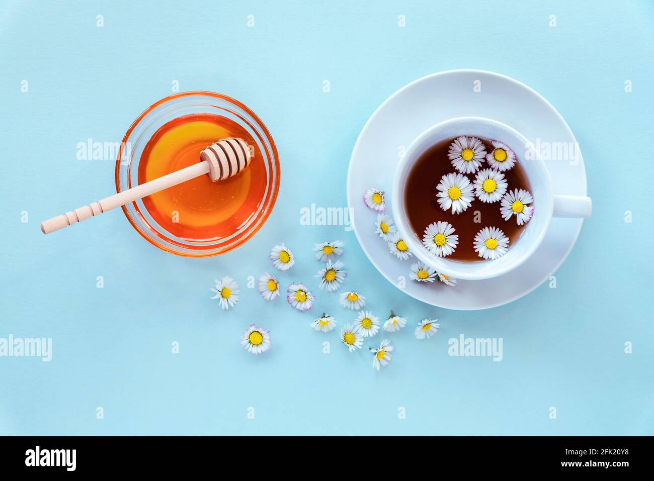 Eine Tasse Tee mit Kamille und Honig in einer Glasschüssel mit einer hölzernen Dipper auf blauem Hintergrund. Draufsicht, flach liegend. Stockfoto