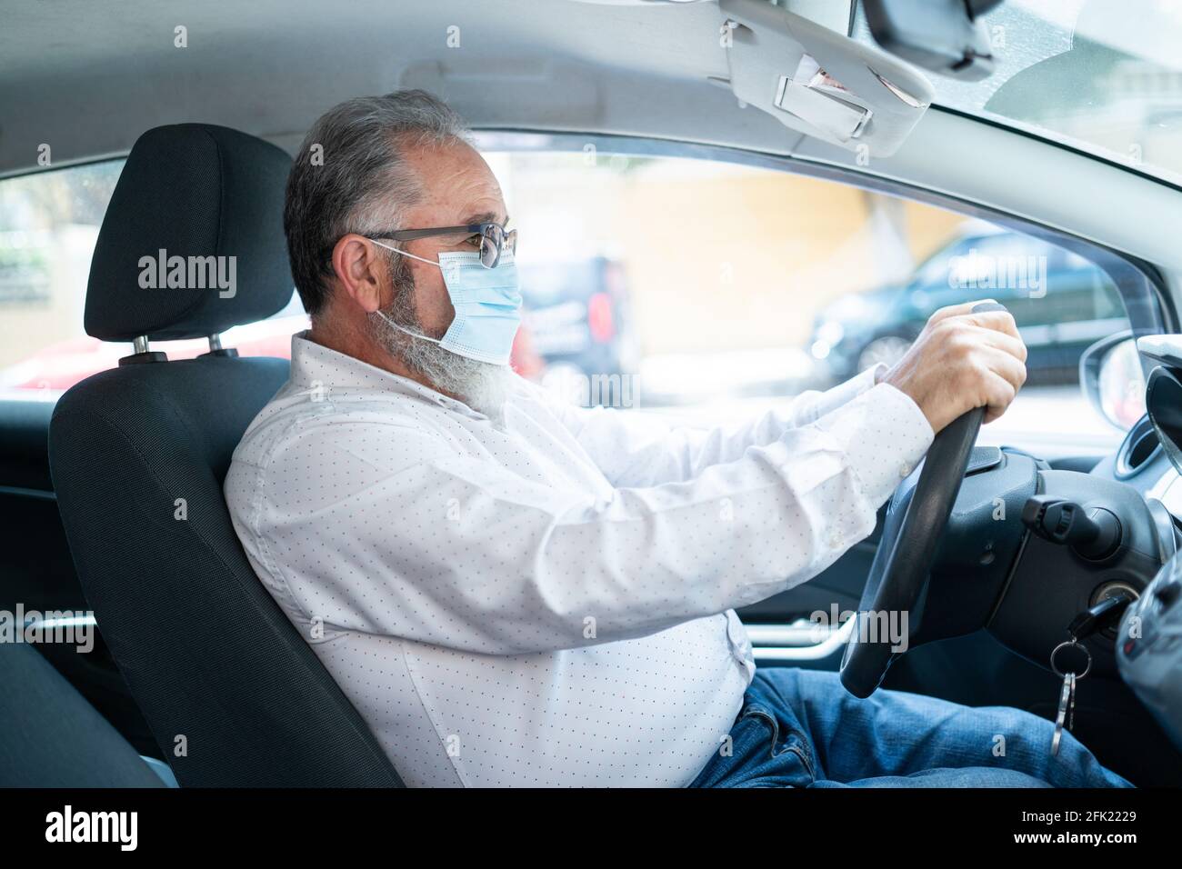 Seitenansicht eines älteren Mannes in einer medizinischen OP-Maske beim Autofahren. Coronavirus-Pandemiekonzept. Stockfoto