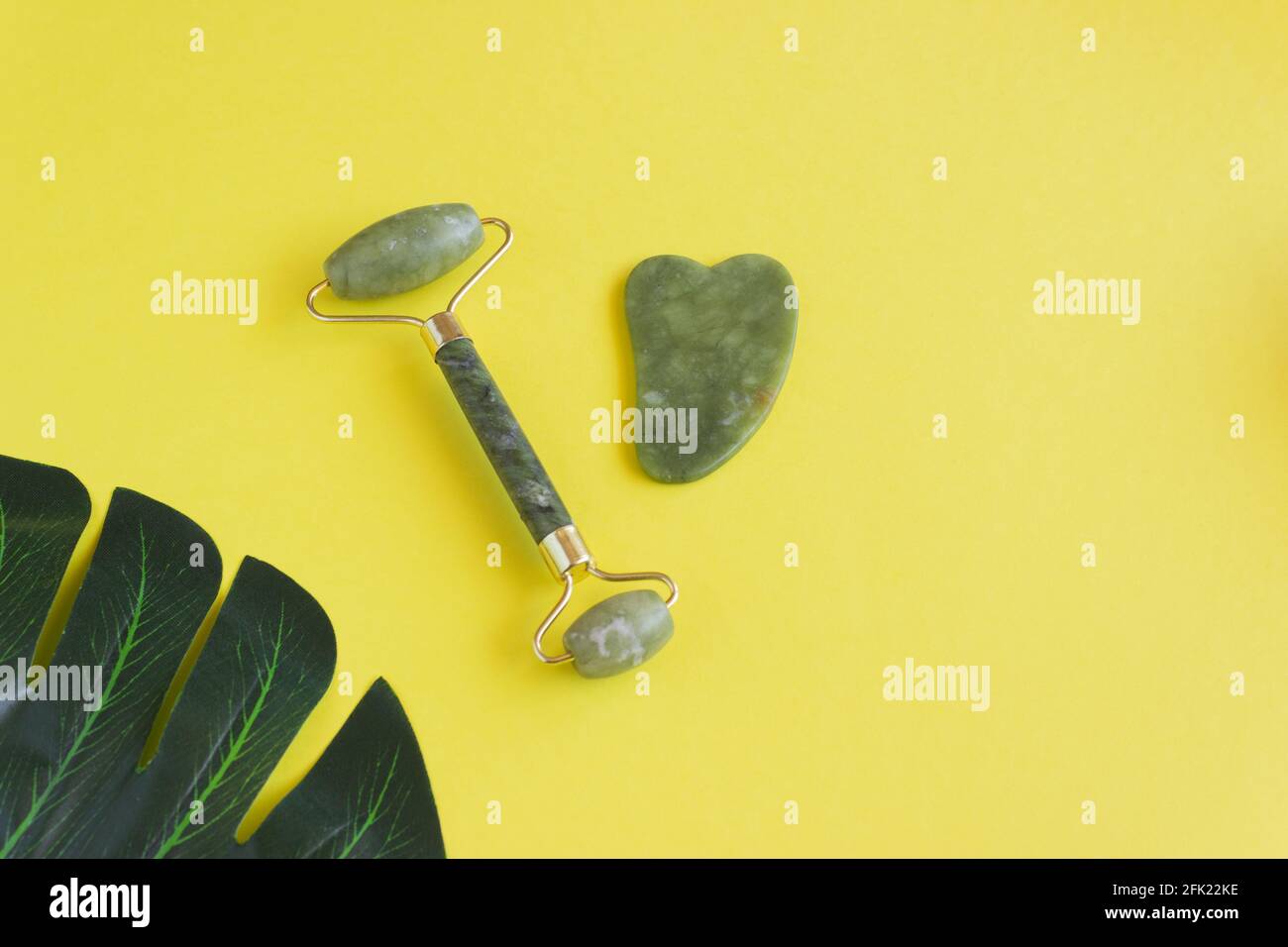 Ein Gua Sha Roller und ein Jadestein-Schaber auf gelbem Hintergrund. Chinesische Massagetechnik Stockfoto