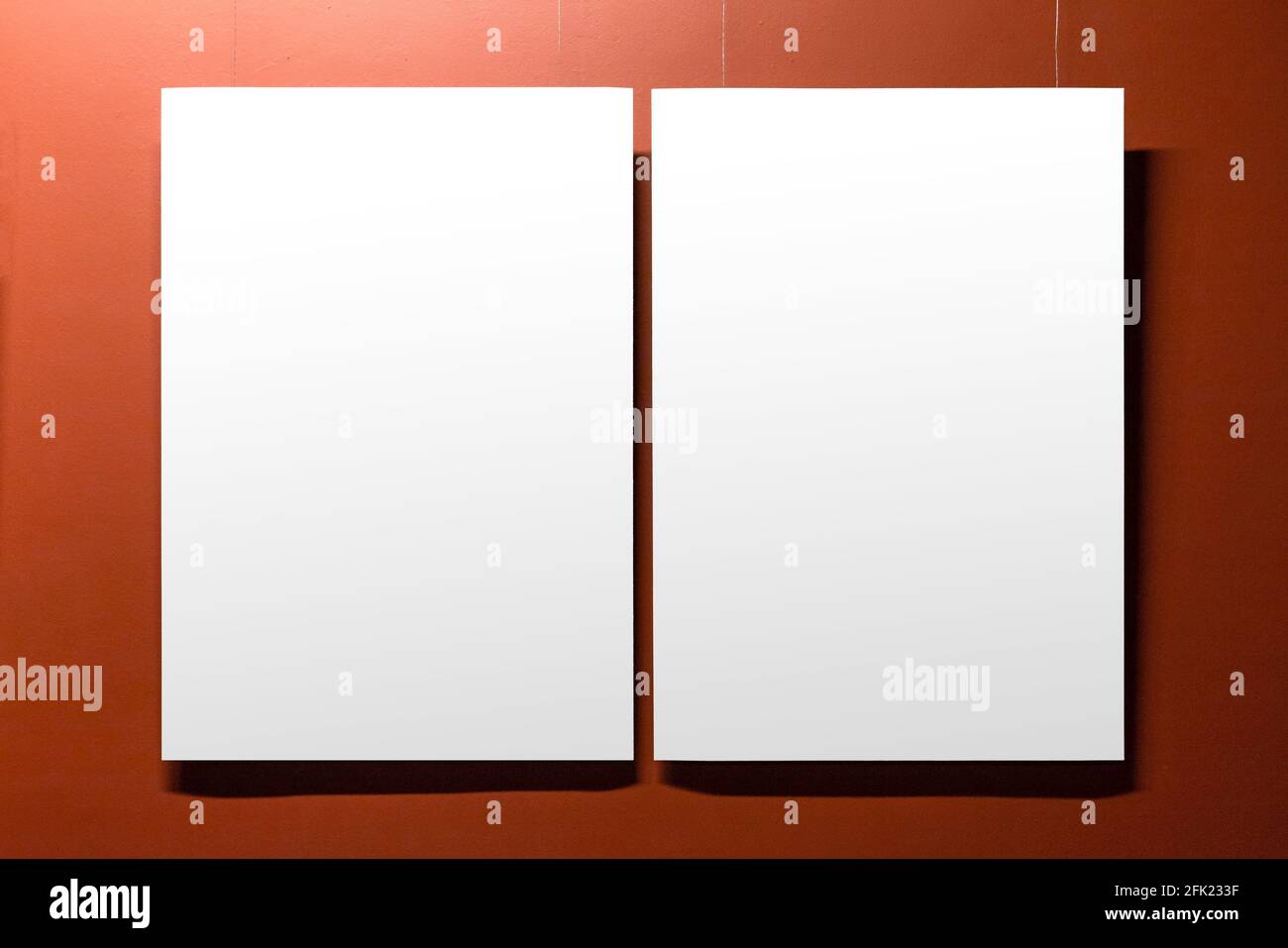An einer roten Wand hängen zwei weiße, leere Poster mit Kopierbereich. Vorderansicht, Hintergrundbild Stockfoto
