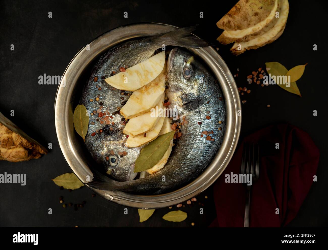 Zwei rohe Brassen in einem Kochtopf auf schwarzem Hintergrund mit Lorbeerblatt, Salz, Knauf Sellerie und schwarzem Pfeffer Dark Mood Fotografie Stockfoto