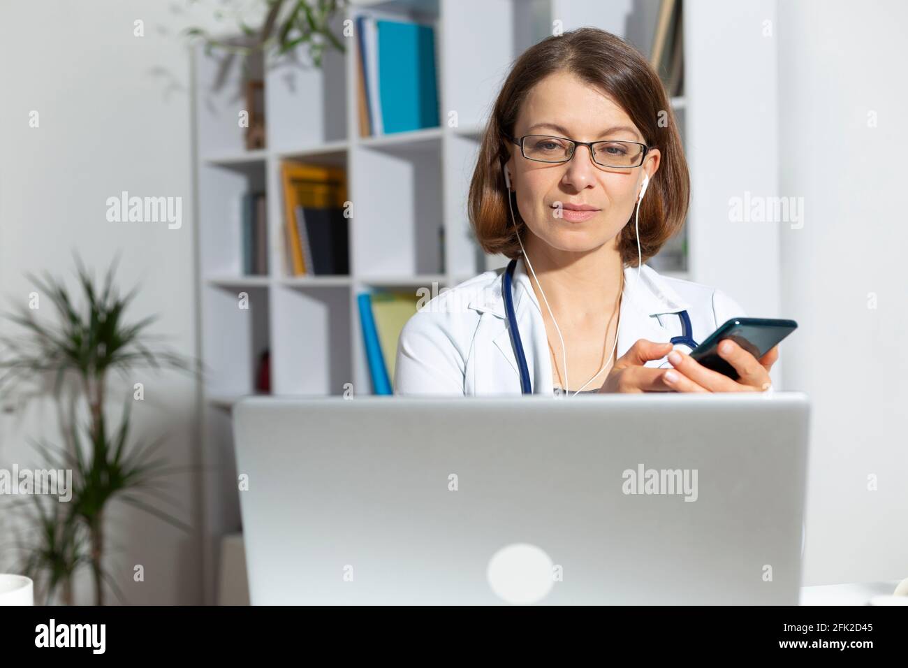 Porträt einer Ärztin, die einen Patienten online per Laptop und Telefon per Fernzugriff konsultiert. Stockfoto