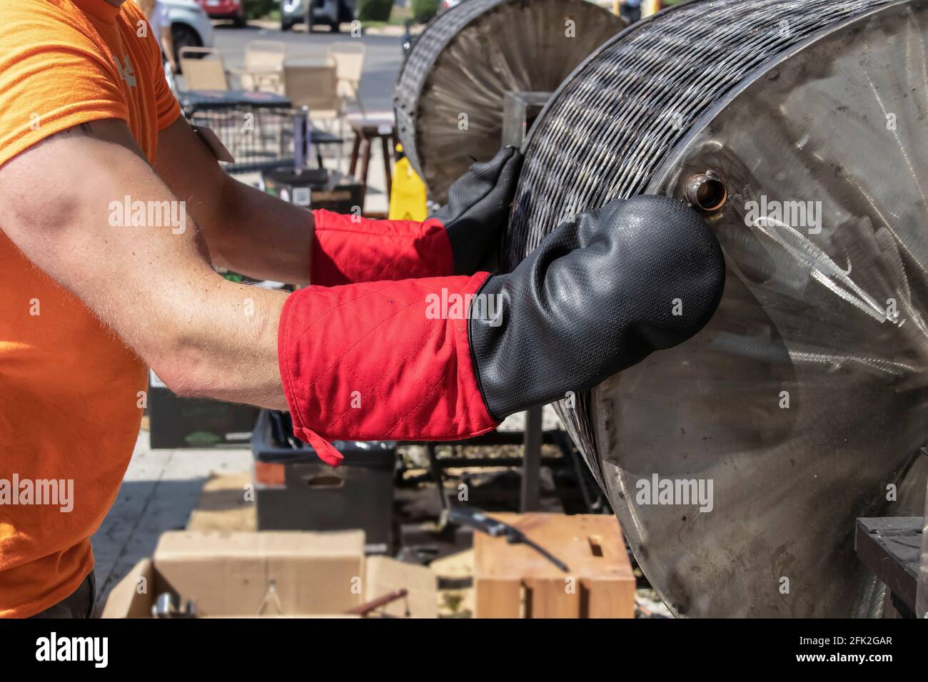 Der Arbeiter stoppt das Drehen des heißen Barrel-Chilischrösters und bereitet es vor Zum Öffnen im Freien mit hochbelastbaren Ofenmits Schlüpfchen der Chilischröstung Stockfoto