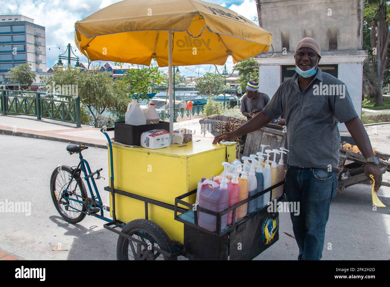 Bridgetown, Barbados - 27 2021. April: Barbados-Mann, der auf der Straße Schneezapfen verkauft, lächelt mit einer Einweg-Gesichtsmaske um sein Kinn. Wirtschaft in Barbados. Stockfoto