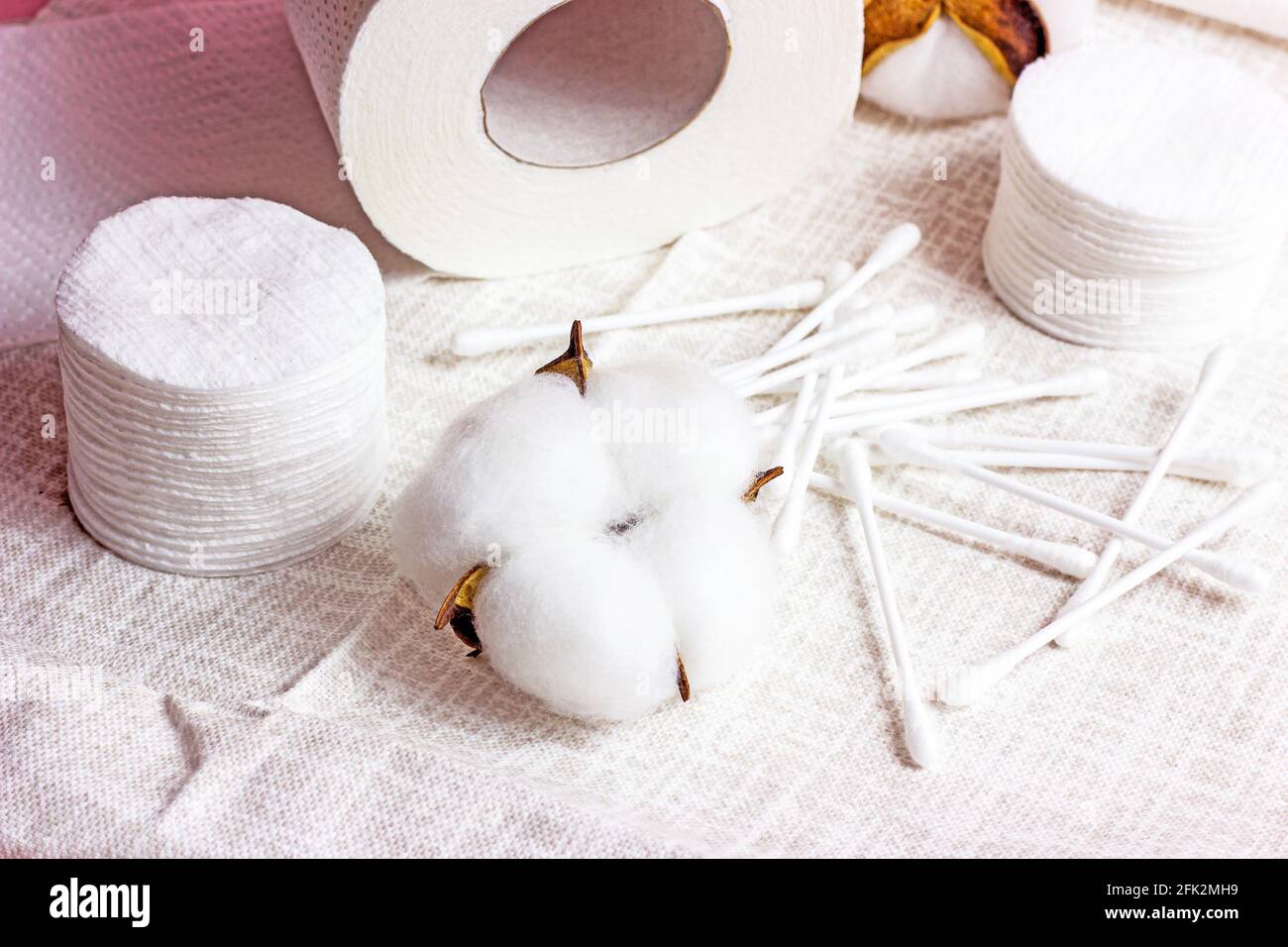 Weiße weiche Wattepads und -Sticks für Hygiene und Gesundheit auf hellem Textilhintergrund. Stockfoto