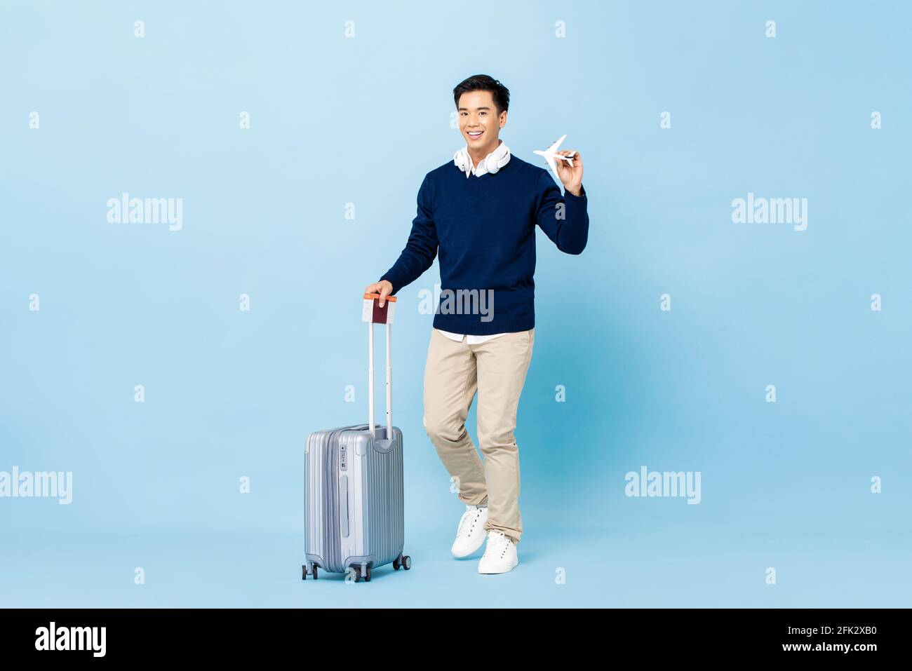 Junger, lächelnder, hübscher asiatischer Tourist mit Gepäck, Reisepass und Bordkarte, der auf hellblauem, isoliertem Studiohintergrund fliegen kann Stockfoto Junger, lächelnder, hübscher asiatischer Tourist mit Gepäck, Reisepass und Bordkarte, der auf hellblauem, isoliertem Studiohintergrund fliegen kann Stockfoto