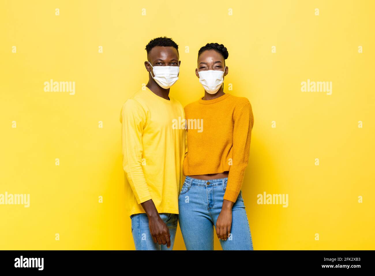 Junges hygienisches afrikanisches Paar mit Gesichtsmaske zum Schutz vor Coronavirus In gelber isolierter Studiohintergrund Stockfoto