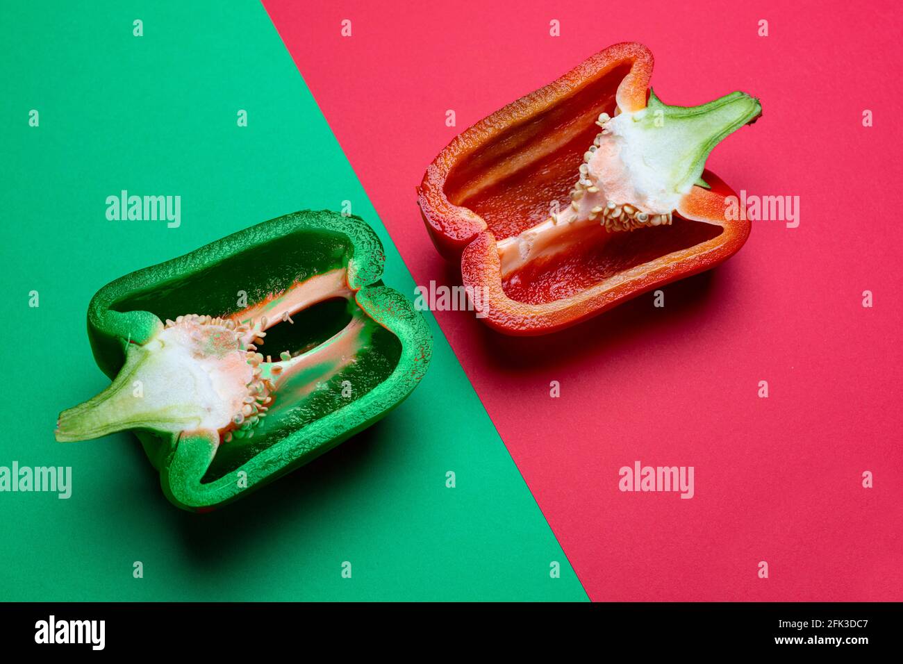 Eine grüne und eine rote Paprika in zwei Hälften geschnitten und Auf einer farbigen Oberfläche angeordnet Stockfoto
