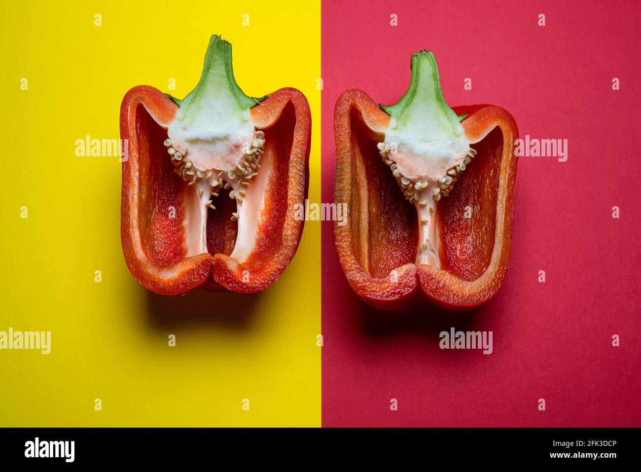 Die rote Paprika in die Hälfte geschnitten und auf a angeordnet Farbige Oberfläche Stockfoto
