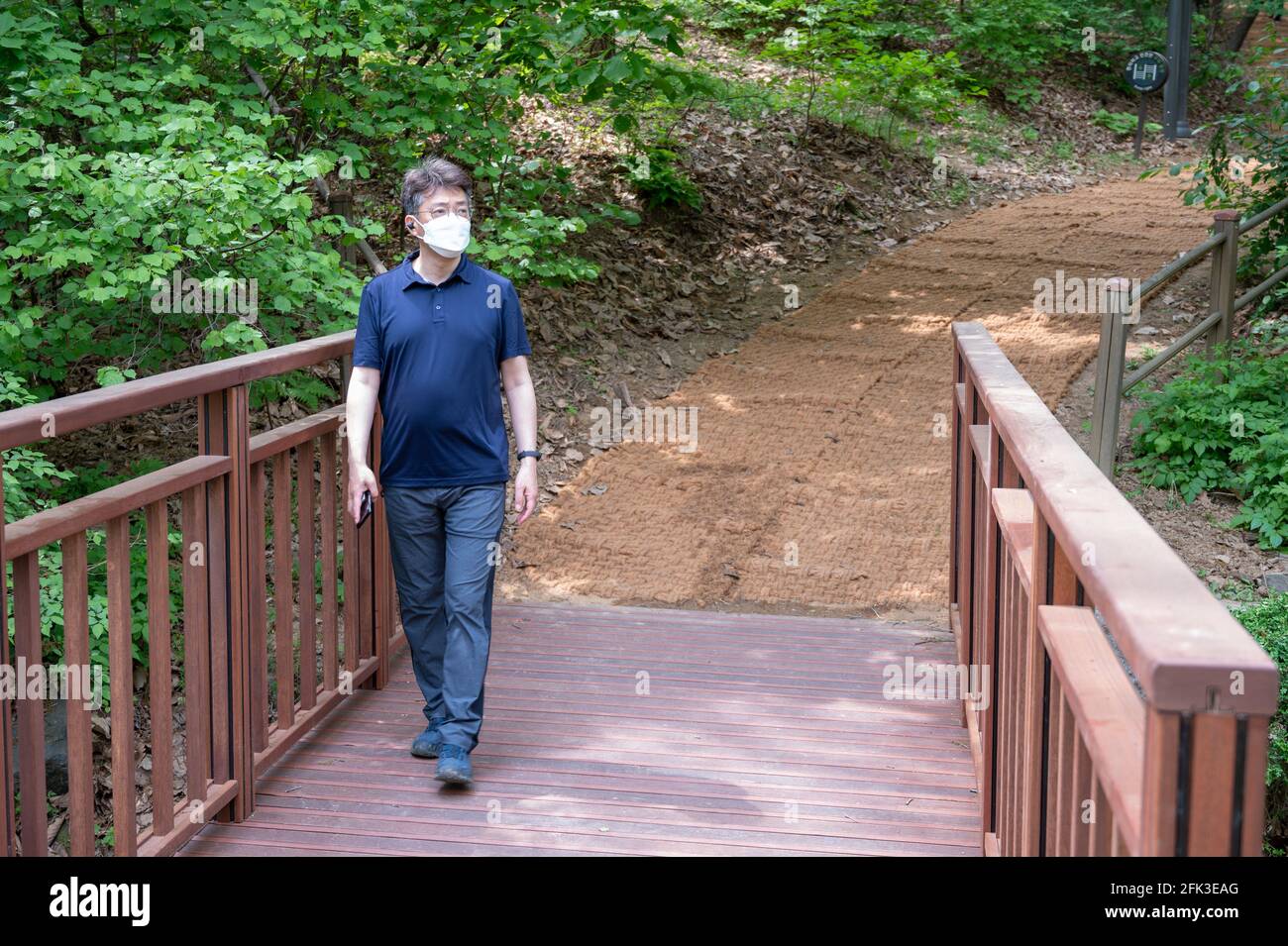 Asiatischer Mann mittleren Alters, der allein in einem Waldweg mit Gesichtsmaske geht. Stockfoto