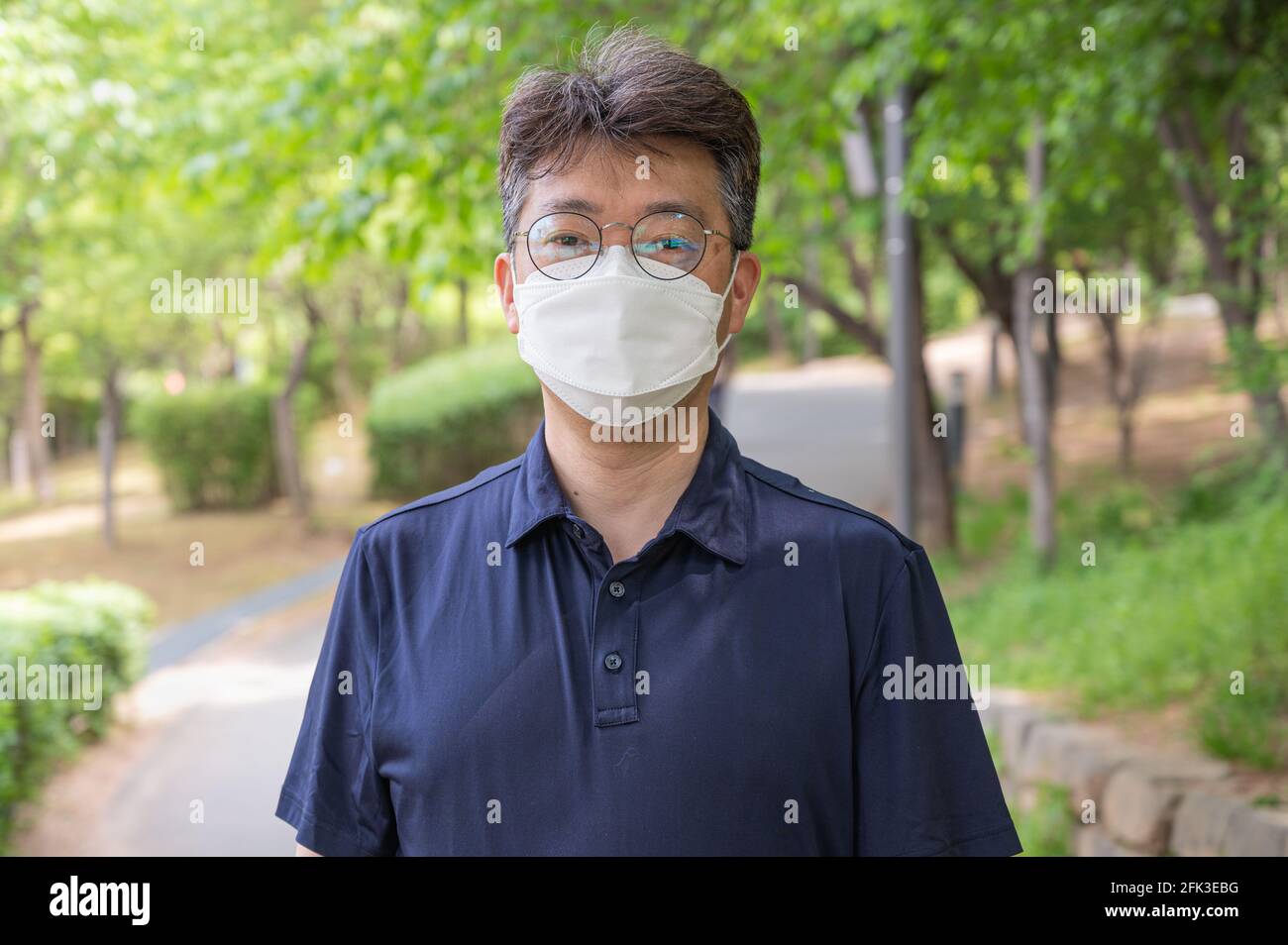 Asiatischer Mann mittleren Alters, der allein in einem Waldweg mit Gesichtsmaske geht. Stockfoto