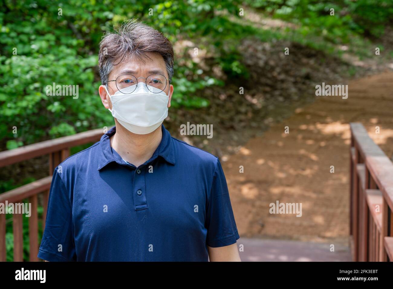 Asiatischer Mann mittleren Alters, der allein in einem Waldweg mit Gesichtsmaske geht. Stockfoto