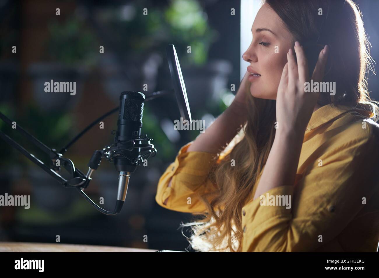 Seitenansicht Nahaufnahme einer attraktiven jungen Frau in modernen Kopfhörern, die in das schwarze Mikrofon singt. Konzept der Aufnahme von trendigen Songs im professionellen Musikstudio. Stockfoto