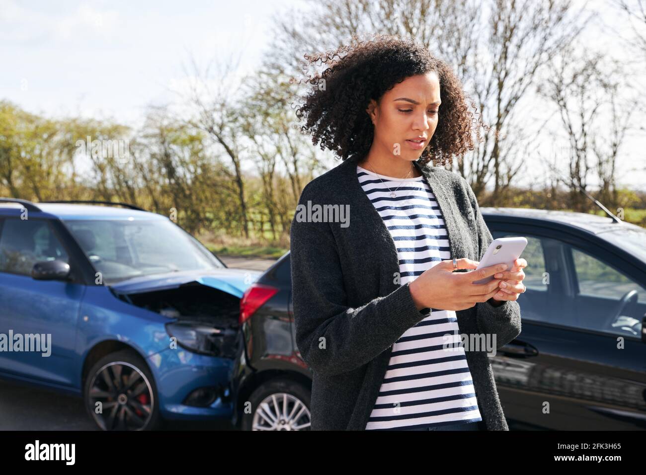 Junge Frau, die nach der Meldung von Verkehrsunfällen an einem beschädigten Auto steht Vorfall bei einer Versicherungsgesellschaft, die ein Mobiltelefon verwendet Stockfoto