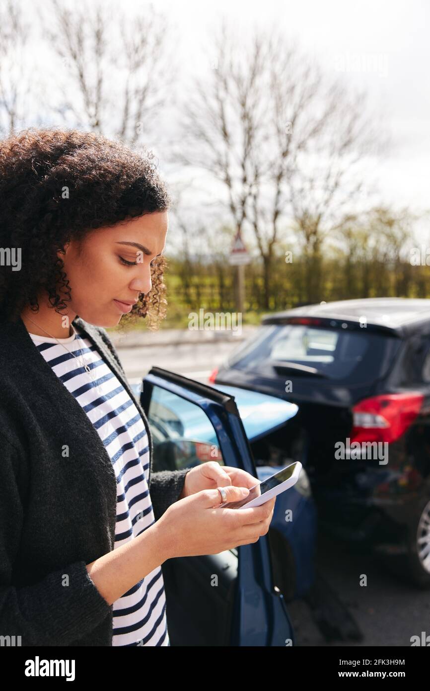 Junge Frau, die nach der Meldung von Verkehrsunfällen an einem beschädigten Auto steht Vorfall bei einer Versicherungsgesellschaft, die ein Mobiltelefon verwendet Stockfoto