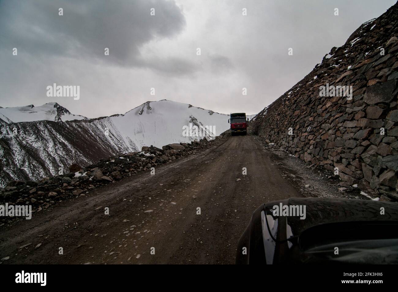 Schwere Lastkraftwagen und Sattelschlepper fahren entlang der unbefestigten Autobahn G216, die Urumuqi mit der Präfektur Bayingolin verbindet, über die schneebedeckten Berge von Tianshan in Xinjiang, China, VR China. © Time-Snaps Stockfoto