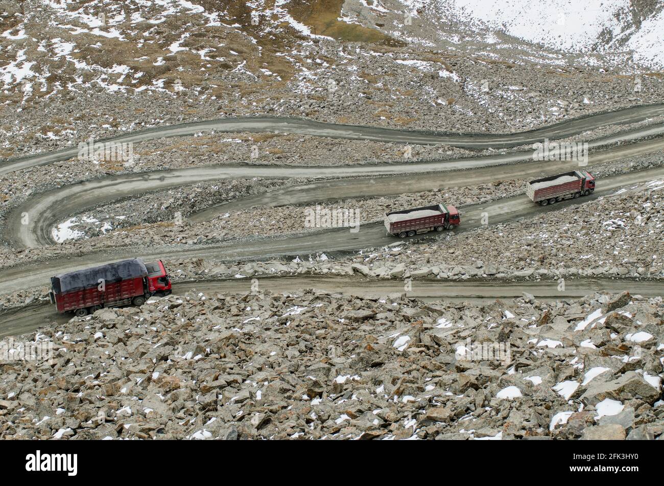 Schwere Lastkraftwagen und Sattelschlepper fahren entlang der unbefestigten Autobahn G216, die Urumuqi mit der Präfektur Bayingolin verbindet, über die schneebedeckten Berge von Tianshan in Xinjiang, China, VR China. © Time-Snaps Stockfoto